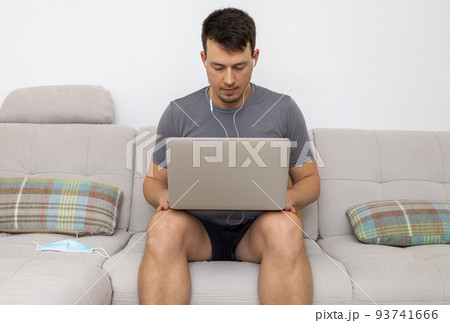 young man in headphones and with laptop sitting on sofa young man in headphones and with laptop sitting on sofa 93741666