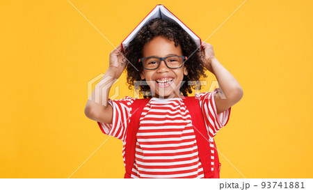 Happy ethnic schoolboy playing with book against yellow background Happy ethnic schoolboy playing with book against yellow background 93741881
