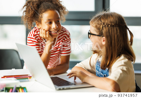Cheerful schoolgirls doing a school assignment using a laptop during online lesson 93741957