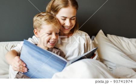 Happy mother and son reading book together on bed 93741974