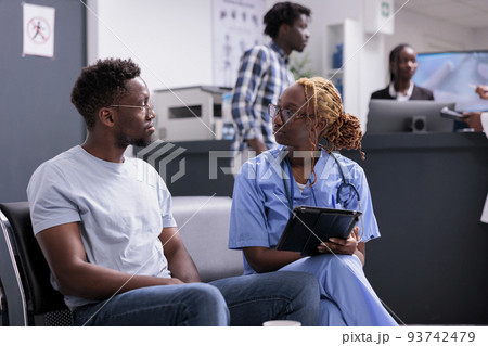 Female nurse doing consultation with patient, taking notes on digital tablet and writing report in waiting room. Medical assistant talking to man, consulting person with disease in waiting area. Female nurse doing consultation with patient, taking notes on digital tablet and writing report in waiting room. Medical assistant talking to man, consulting person with disease in waiting area. 93742479