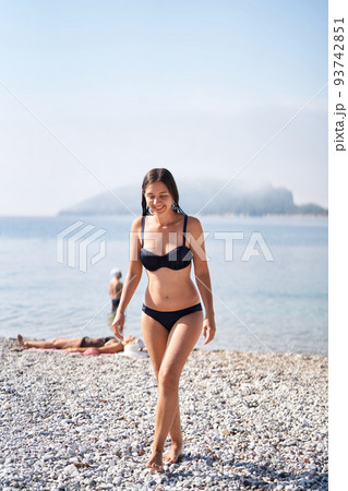 Young smiling girl in a bikini comes out of the water Young smiling girl in a bikini comes out of the water 93742851