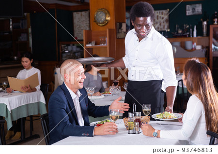 African American waiter bringing ordered dishes to couple African American waiter bringing ordered dishes to couple 93746813