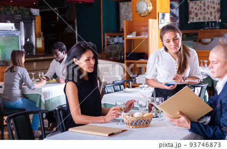 smiling female waiter taking order from adult man and woman in restaurante smiling female waiter taking order from adult man and woman in restaurante 93746873