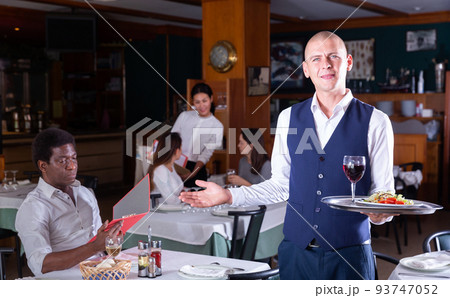 portrait of smiling male waitress standing in modern restaurante portrait of smiling male waitress standing in modern restaurante 93747052
