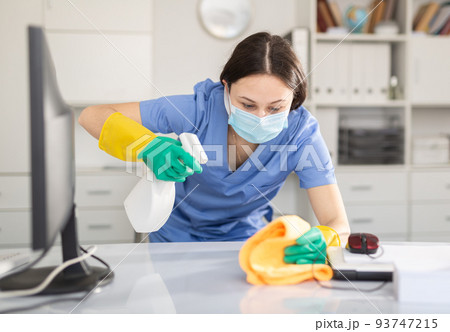 Young woman in a protective mask, cleaning the office, wipes the desktop Young woman in a protective mask, cleaning the office, wipes the desktop 93747215