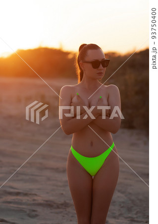 Fit sexy lady in bikini covering breast on sandy seashore at sundown Fit sexy lady in bikini covering breast on sandy seashore at sundown 93750400