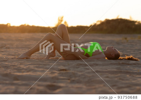 Sexy fit woman relaxing on sandy shore at sundown Sexy fit woman relaxing on sandy shore at sundown 93750688