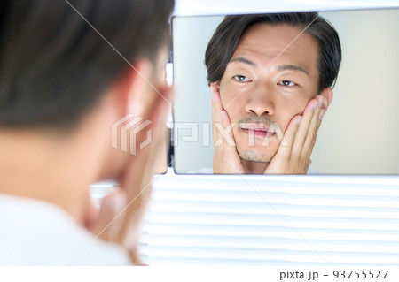 疲れた顔で鏡を見る若い男性 93755527