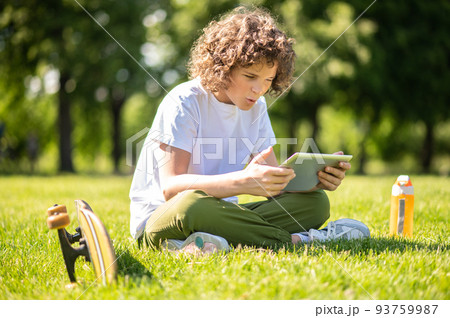 Teen involved in watching a video outdoors Teen involved in watching a video outdoors 93759987