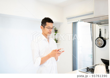 キッチンでスマホを使って調べ物をしている男性 93761390