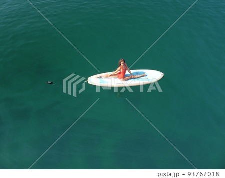Aerial drone view on well looking middle aged woman with black hair in red swimsuit, swimming on sup in calm azure sea. Summer holiday vacation and travel concept. Aerial drone view on well looking middle aged woman with black hair in red swimsuit, swimming on sup in calm azure sea. Summer holiday vacation and travel concept. 93762018