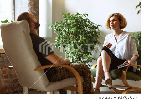 Sad young man in military uniform at therapy session with female psychiatrist, indoors. Concept of mental health, post-traumatic syndrome, help and support Sad young man in military uniform at therapy session with female psychiatrist, indoors. Concept of mental health, post-traumatic syndrome, help and support 93765657