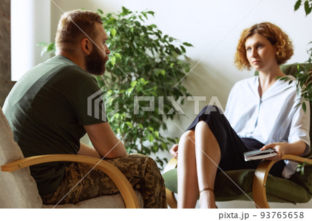 Young distressed man in military uniform talking to psychologist during therapy session, indoors. Help, support, ptsd, health and harmony concept Young distressed man in military uniform talking to psychologist during therapy session, indoors. Help, support, ptsd, health and harmony concept 93765658