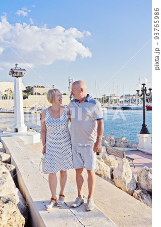 Middle-aged couple of baby boomers people posing for photograph opposite blue sea Middle-aged couple of baby boomers people posing for photograph opposite blue sea 93765986