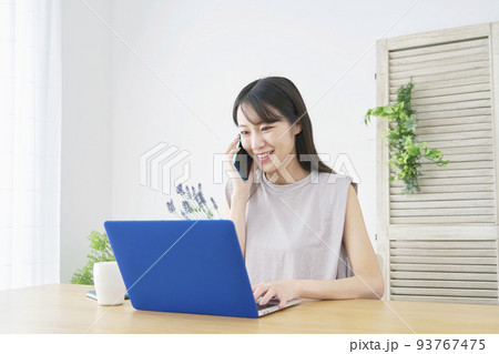 リビングでノートパソコンを見てスマホで電話する女性 リビングでノートパソコンを見てスマホで電話する女性 93767475