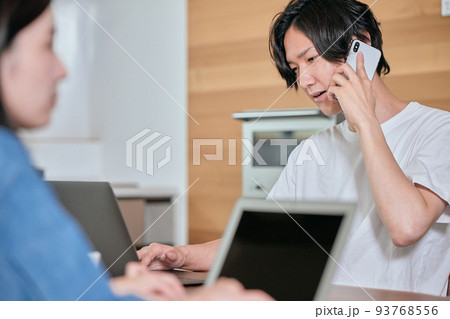 テレワーク中にスマホで電話をする若い男性 93768556