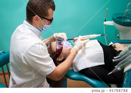 Dentist using whitening ultraviolet lamp on her teeth. Young girl patient at the dental clinic lies in uv glasses on the dentist's chair.. Dentist using whitening ultraviolet lamp on her teeth. Young girl patient at the dental clinic lies in uv glasses on the dentist's chair.. 93768788