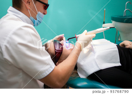 Dentist using whitening ultraviolet lamp on her teeth. Young girl patient at the dental clinic lies in uv glasses on the dentist's chair.. 93768790