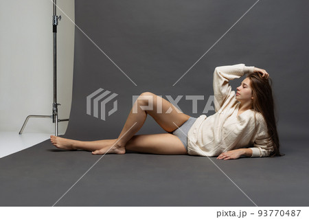 Studio shot of charming girl with long glossy hair wearing sweater and underwear isolated over gray background. 93770487
