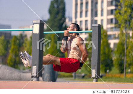 Workout. Strong muscular man, student training, practicing at sport ground at public park in summer morning, outdoors. Action, skills, challenges Workout. Strong muscular man, student training, practicing at sport ground at public park in summer morning, outdoors. Action, skills, challenges 93772528