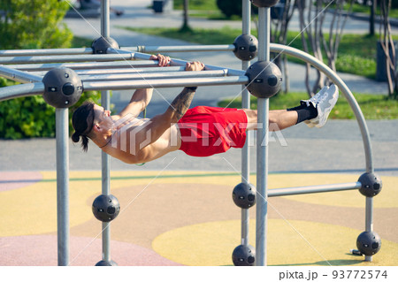 Young strong muscular man doing strength exercises on workout ground at public park in summer morning. Sport, fitness, healthy lifestyle concept 93772574