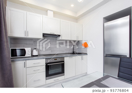 Clean kitchen in a small cozy contemporary studio apartment. Table and chairs in the foreground. Built in household appliance 93776804