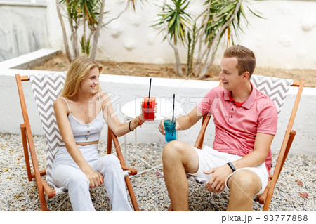 Happy young couple with glasses of lemonade sitting on deck chairs at sea beach or cafe place. Happy young couple with glasses of lemonade sitting on deck chairs at sea beach or cafe place. 93777888
