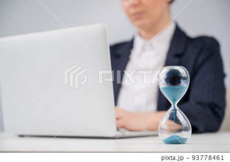 Business woman keeps track of time on an hourglass while working. 93778461