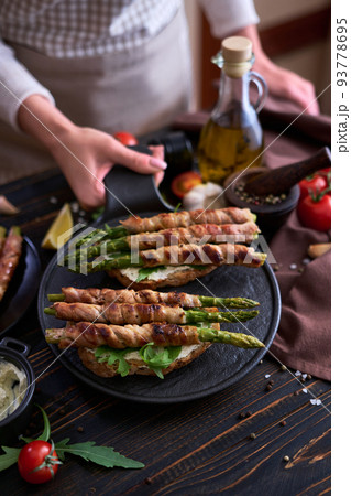 Tasty breakfast - toasts with cream cheese and Asparagus wrapped with bacon and spices on a plate Tasty breakfast - toasts with cream cheese and Asparagus wrapped with bacon and spices on a plate 93778695