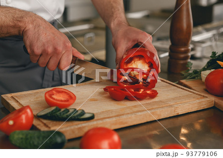 Busy chef cutting red pepper and cucumbers on a board for making salad in modern restaurant kitchen 93779106