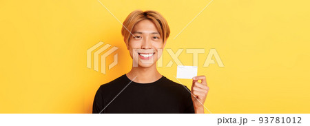 Close-up of handsome pleased asian guy with fair hair, smiling happy and showing credit card over yellow background Close-up of handsome pleased asian guy with fair hair, smiling happy and showing credit card over yellow background 93781012