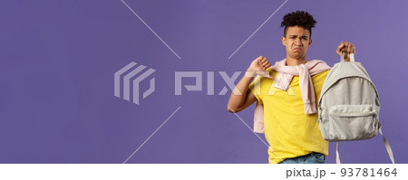 Education, university and trends concept. Portrait of gloomy disappointed young male student complaining on ugly new backpack, show thumbs-down and grimacing displeased, purple background 93781464