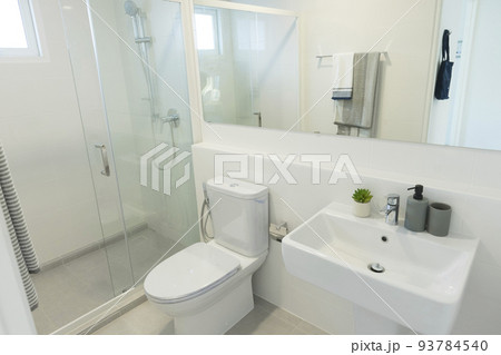 Modern toilet and ceramic sink installed on white tiled walls near mirror and towel in restroom at home 93784540