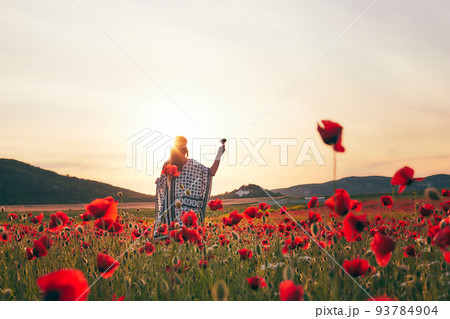 A woman eating strawberries at sunset in a field of poppies. Front view. 93784904