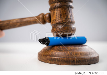 Judge hammering disposable vape with referee's gavel on white table.  93785900