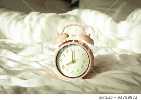 Pink alarm clock on the bed in the morning Pink alarm clock on the bed in the morning 93789972
