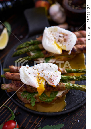 Tasty breakfast - toasts with cream cheese, poached eggs and Asparagus wrapped with bacon and spices on a plate 93791122