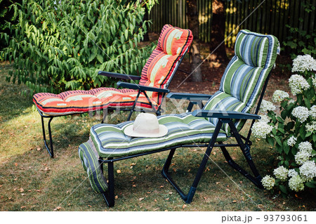 Two soft sun loungers with straw hat in inner courtyard. Two empty sun beds in a sunny garden for relaxation. 93793061