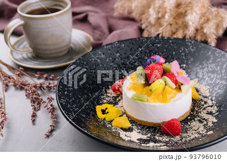 Round cheesecake with fruit decoration and cup of coffee 93796010