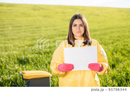 Person in overalls holds paper with blank sheet of paper for text inscription while standing on green field. Concept of bad ecology and environmental protection Person in overalls holds paper with blank sheet of paper for text inscription while standing on green field. Concept of bad ecology and environmental protection 93796344