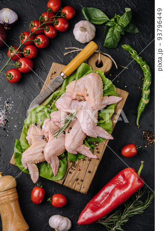 Raw chicken wings with ingredients for cooking on a wooden cutting board over dark stone background Raw chicken wings with ingredients for cooking on a wooden cutting board over dark stone background 93796449