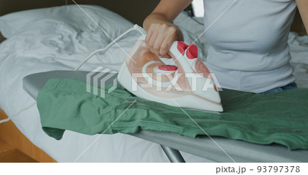 Woman iron clothes with iron on ironing board 93797378