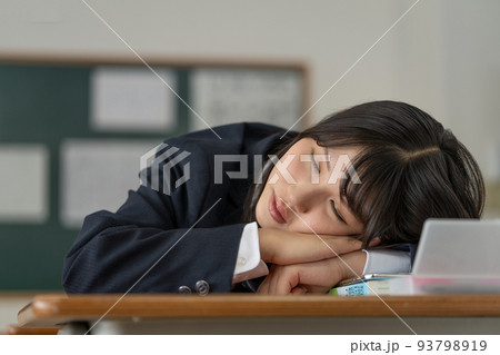 学校の休み時間に机に伏せて寝る女子高生 93798919