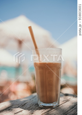 Ice coffee latte in tall glass with straw by the sea in beach bar Ice coffee latte in tall glass with straw by the sea in beach bar 93803601