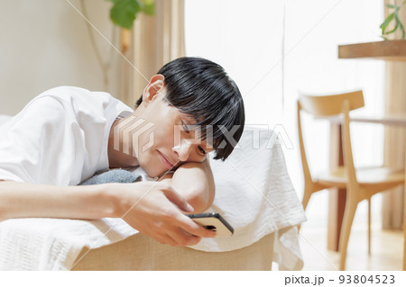 ソファーでだらけながらスマホを見る男性 93804523