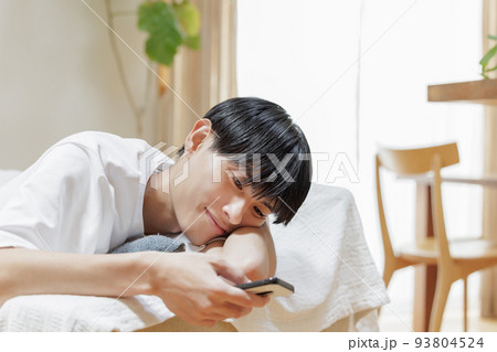 ソファーでだらけながらスマホを見る男性 93804524