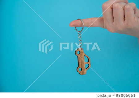 Woman's hand holding a wooden keychain in the shape of a car on a blue background. 93806661
