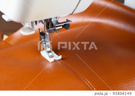 Modern sewing machine presser foot with a needle sews brown leather Modern sewing machine presser foot with a needle sews brown leather 93808149