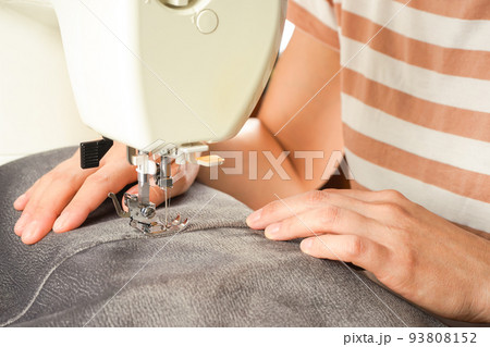 Female hands stitching gray fabric on modern sewing machine. Close up view of sewing process. Female hands stitching gray fabric on modern sewing machine. Close up view of sewing process. 93808152